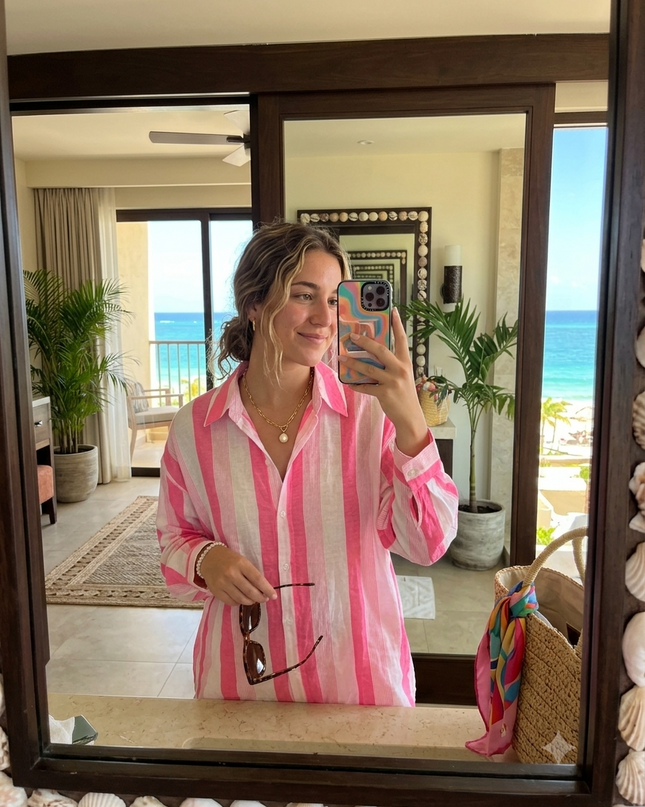 Sagar hill road relaxed cotton shirt with pink and white vertical stripes, worn by a woman in a beach resort mirror.